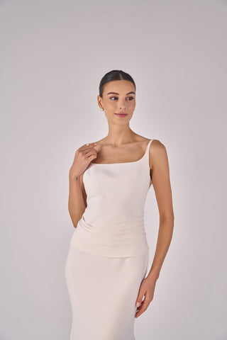 Woman wearing a white sleeveless top and skirt on a plain background