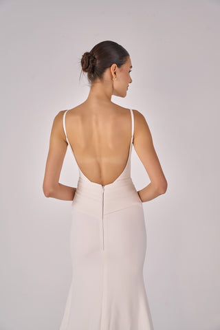 Woman wearing a white gown with an open back on a plain background