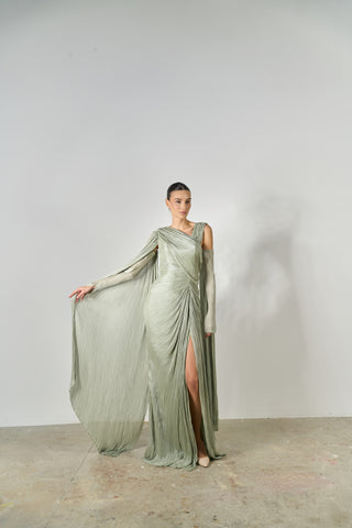 Woman wearing a long, flowing green dress with a slit on a plain background