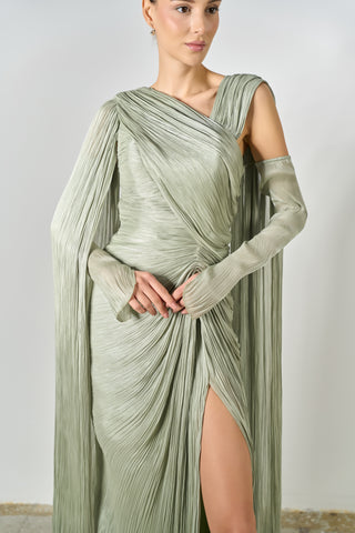 Woman wearing a green draped dress with a slit on a plain background