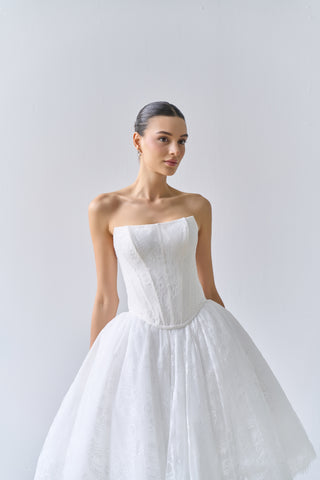 Woman wearing a strapless white wedding dress against a plain background