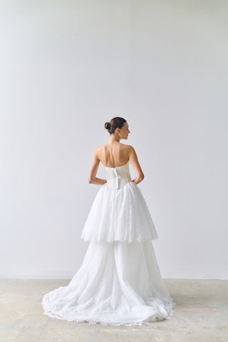 Woman wearing a white strapless gown with a bow detail on a plain background