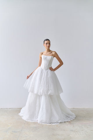 Woman wearing a strapless white wedding dress against a plain background