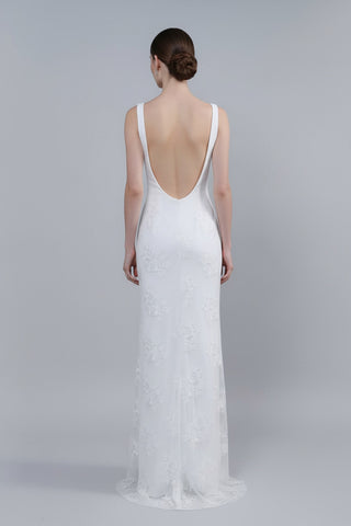 Woman wearing a white lace wedding dress with an open back on a plain background