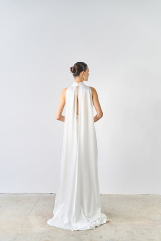 Woman wearing a long white dress with a high slit on a plain background