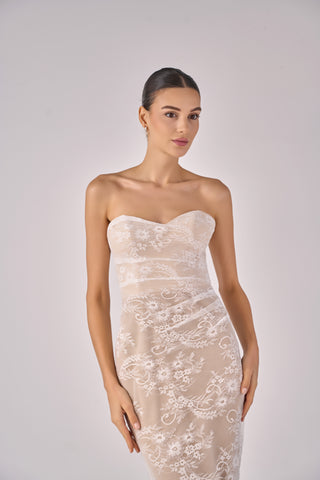 Woman wearing a strapless lace dress against a plain background