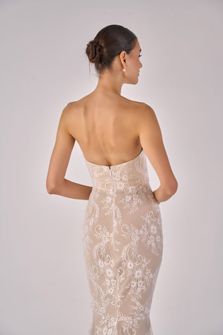 Woman wearing a beige strapless lace dress on a plain background