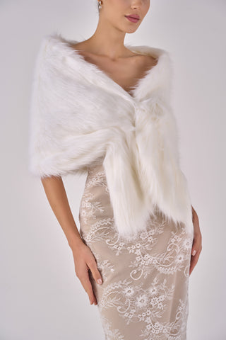 Woman wearing a white fur shrug over a beige dress with floral patterns on a plain background