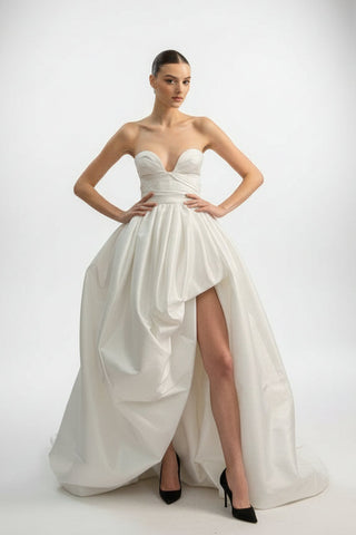 Model wearing a white strapless gown with a high slit on a white background