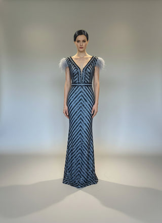 Woman wearing a black and white patterned evening gown with feathered shoulders on a plain background