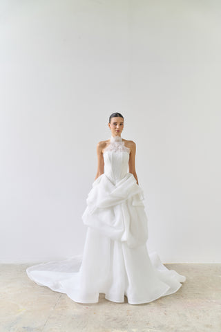 Woman wearing a white wedding dress with a large train on a plain background