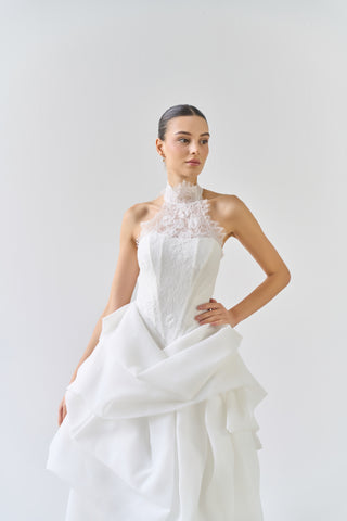 Woman wearing a white wedding dress with floral details on a plain background