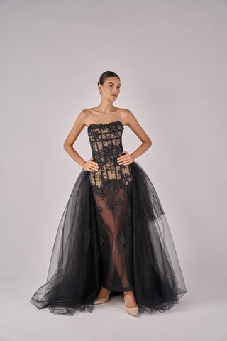 Woman wearing a black lace dress with a sheer overlay on a gray background