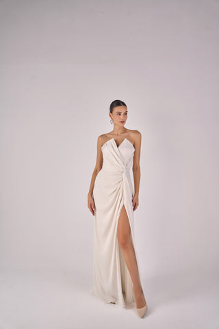 Woman wearing a white strapless gown with a high slit on a plain background