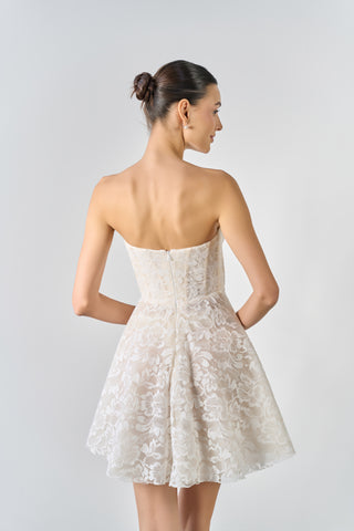 Woman wearing a strapless lace dress against a plain background