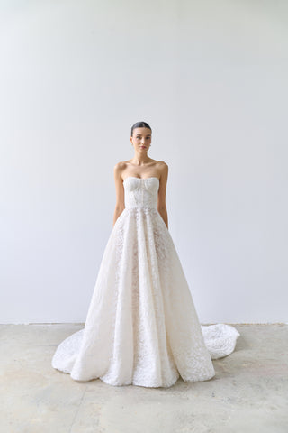 Woman wearing a strapless white lace wedding dress against a plain background