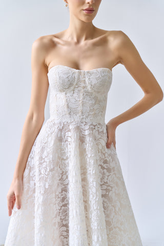 Woman wearing a strapless lace wedding dress against a plain background