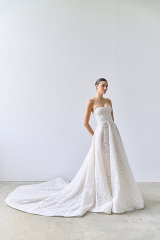 Woman wearing a strapless lace wedding dress with a long train on a plain background