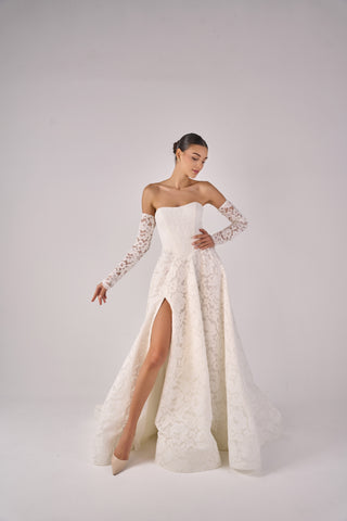 Woman wearing a white lace wedding dress with long sleeves on a plain background