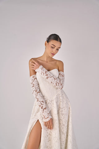 Woman wearing a white lace off-shoulder dress against a plain background