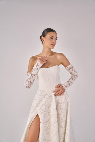 Woman wearing a white lace dress with long sleeves on a plain background
