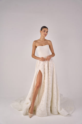 Woman wearing a strapless white wedding dress with a high slit on a plain background