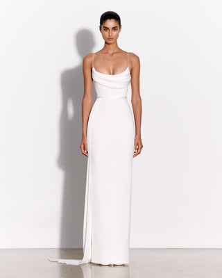 Model wearing the Margot wedding dress by Alex Perry, standing against a white background. The gown features a draped neckline, thin straps, and a sleek, floor-length silhouette in satin crepe.