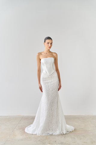 Woman wearing a strapless lace wedding dress against a plain background