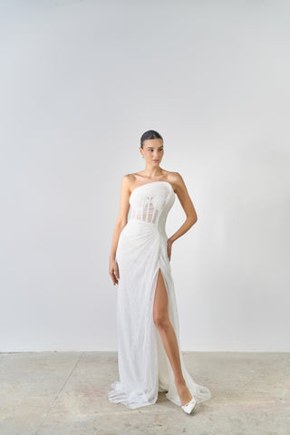 Woman wearing a white strapless gown with a high slit on a plain background