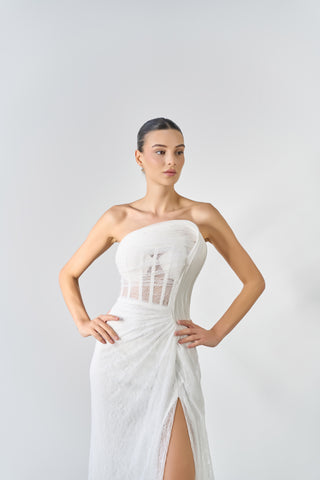 Woman wearing a white strapless dress with mesh panels on a plain background