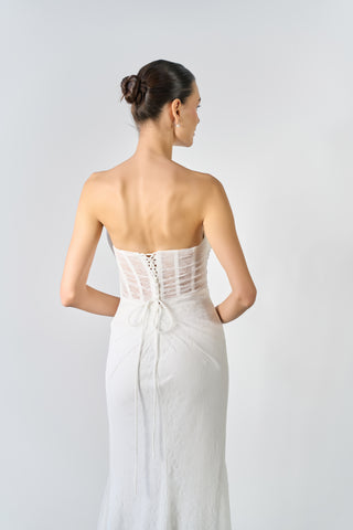 Woman wearing a white strapless dress with a lace-up back on a plain background