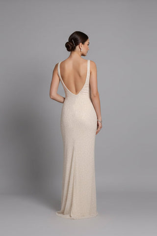 Woman wearing a beige evening gown with a low back on a gray background