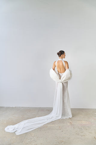 Woman wearing a white wedding dress with a long train against a plain background