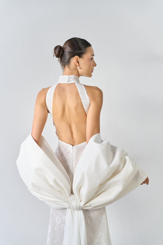 Woman wearing a white halter neck dress with a large bow at the back on a plain background