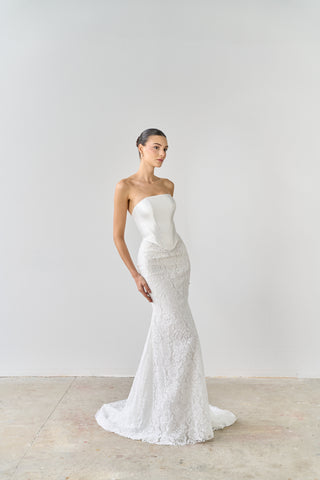 Woman wearing a white strapless wedding dress against a plain background