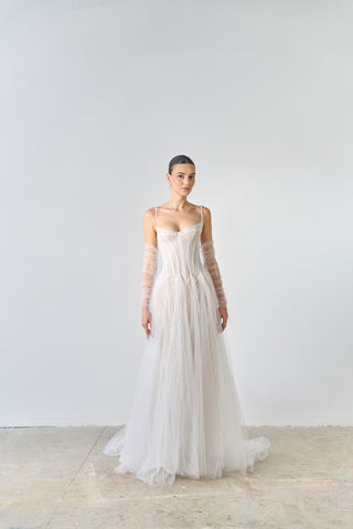 Woman wearing a white wedding dress with sheer sleeves against a plain background