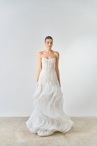 Woman wearing a strapless white wedding dress against a plain background