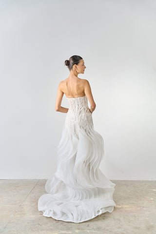 Woman wearing a strapless white wedding dress with a flowing train on a plain background