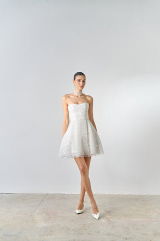 Woman wearing a strapless white dress against a plain background