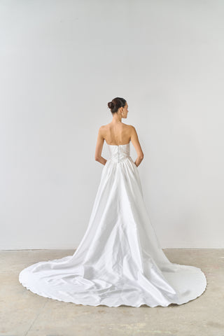 Woman wearing a white wedding dress with a long train on a plain background
