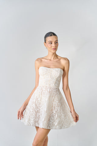 Woman wearing a strapless white lace dress against a plain background