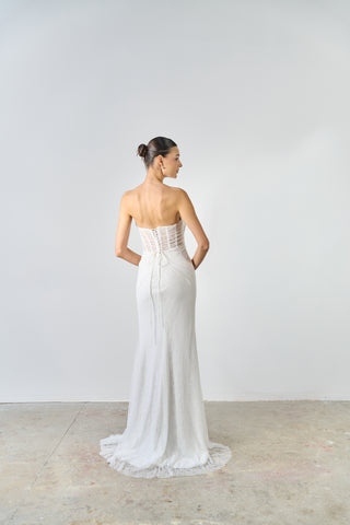 Woman wearing a white strapless gown with a fitted bodice and flowing skirt against a plain background.