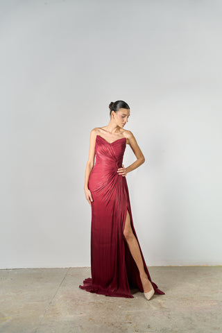 Woman wearing a burgundy evening gown with a slit on a plain background