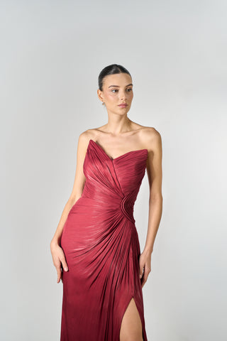 Woman wearing a burgundy one-shoulder dress with a slit on a light gray background