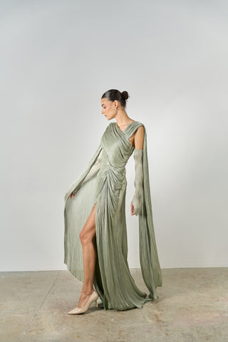 Woman wearing a long, flowing green dress with a slit on a plain background