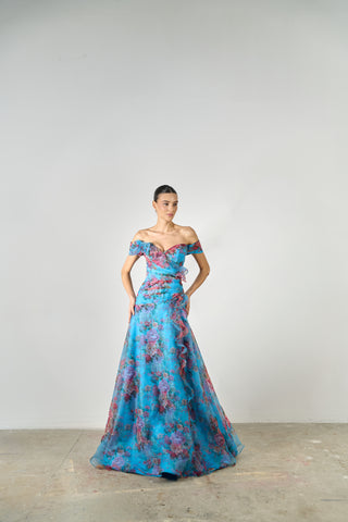 Woman wearing a blue floral off-shoulder gown against a plain background