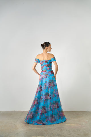 Woman wearing a blue floral off-shoulder gown against a plain background