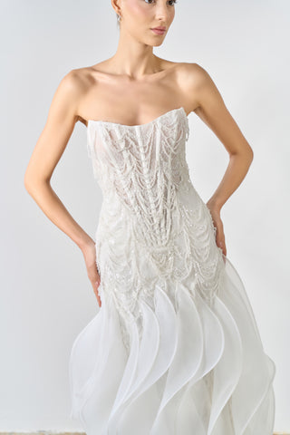 Woman wearing a strapless white wedding dress against a plain background