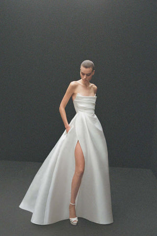 Model wearing the Olivia by Alex Perry, a white strapless silk faille gown featuring a curved neckline, draped bodice, and a thigh-high slit in the full skirt.