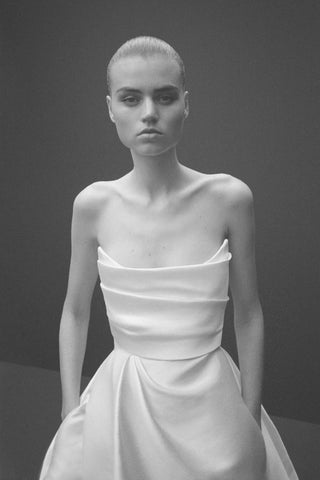 Waist-up view of a model in the Olivia Curved Strapless Draped Corset Gown by Alex Perry, with hands in the concealed pockets, highlighting the gown’s elegant draping.